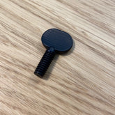 A small, black Schacht Tensioned Lazy Kate Thumb Screw from Schacht Spindle Co. with a wide, ridged, round head and a threaded shaft lies on a light wood surface with visible grain patterns. Perfect as a replacement thumb screw for Tensioned Lazy Kates.