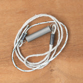 A Schacht Tension Spring and String, produced by Schacht Spindle Co., featuring a coiled metal spring connected to a white rope with metal clasps, rests on a wooden surface.