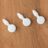 Three Schacht Arrow Pegs from Schacht Spindle Co., made of white plastic, are artfully arranged diagonally on a wooden surface, reminiscent of the precision seen in Table Looms.