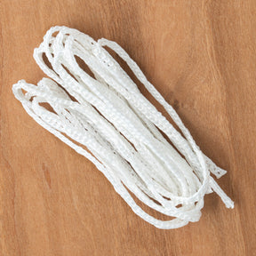 A pack of Schacht Table Loom Lever Cords by Schacht Spindle Co., evocative of white shoelaces, is neatly arranged on a wooden surface. The cords have a braided texture and are slightly overlapping each other.