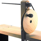 The Louët - Single-Ended Hand Winder by Louët Inc. features a wooden spinning wheel with a circular wheel and handle, mounted on a wooden surface. A black metal arm extends horizontally from the top, making it ideal for tasks such as winding yarn or string.