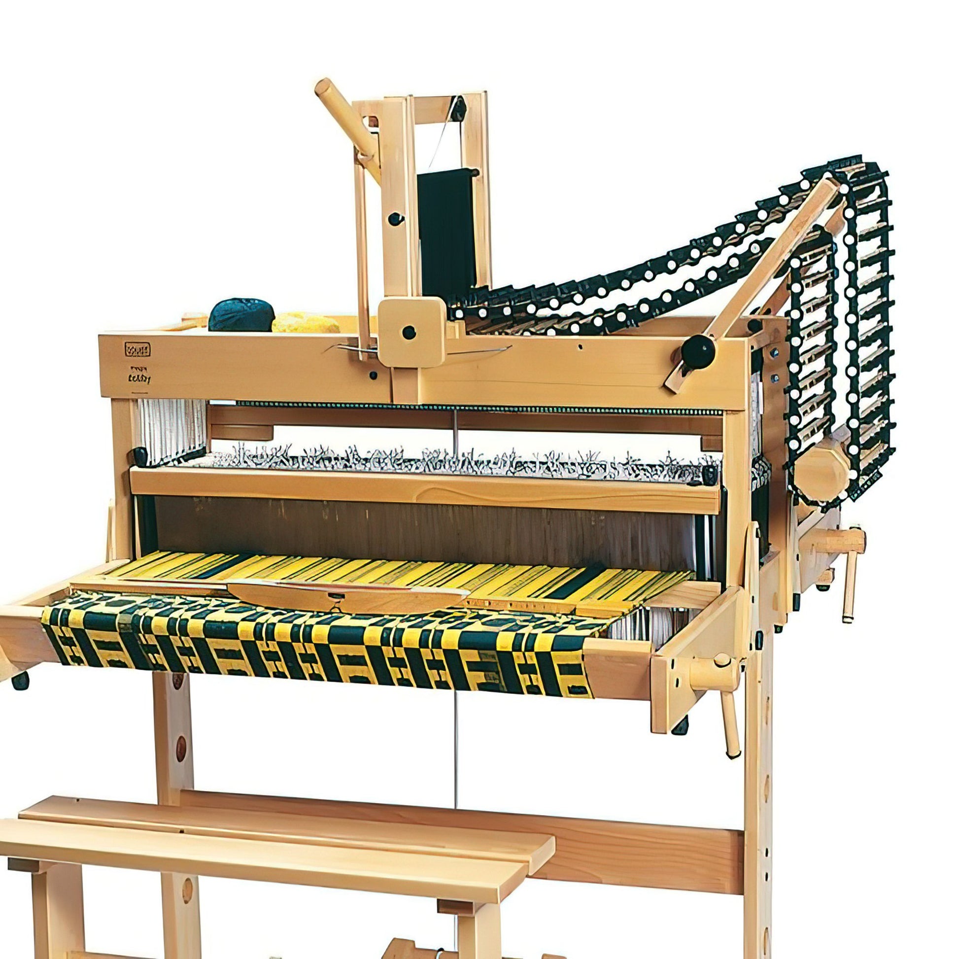 A Louët Magic Dobby 24-shaft Floor Loom without Dobby Control Head by Louët Inc. showcasing a partially woven textile in black, green, and yellow. Several spools of yarn are visible on top, and a wooden bench is partially visible beneath the loom. The loom appears complex with multiple mechanisms and threads in place.