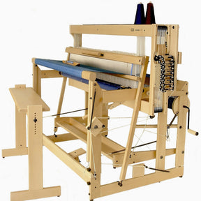 A Louët Octado 8-shaft Floor Loom without Dobby Control Head from Louët Inc. with blue fabric partially woven on it. The loom features various levers, strings, and pulleys, along with yarn cones placed on top. Attached to the side is a wooden bench for the weaver to sit on.