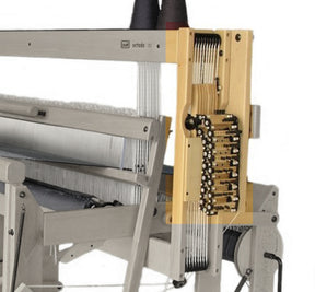 A close-up view of a Louët Octado 8 Shaft Mechanical Dobby Head by Louët Inc. showing its intricate mechanical components. The loom features wooden and metallic parts with vertically running threads, enhanced by an electric dobby. The device appears to be used for weaving textiles, with various threads and levers visible.
