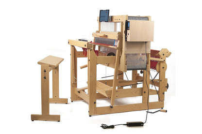 The Louët Megado Floor Loom without Dobby Control Head, crafted by Louët Inc., is an electric wooden loom featuring multiple heddles and a control panel. It includes an adjustable wooden stool and comes equipped with various levers, pedals, and a power cord connected to an adapter on the floor.