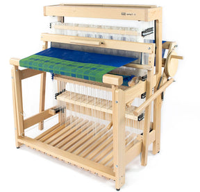 The Louët Spring 2, 8-shaft Floor Loom by Louët Inc. showcases a wooden construction adorned with various strings and a partially completed fabric in shades of blue and green. This well-crafted loom includes numerous weaving mechanisms, featuring a sturdy frame along with various levers and pedals for precise control of the weaving process.