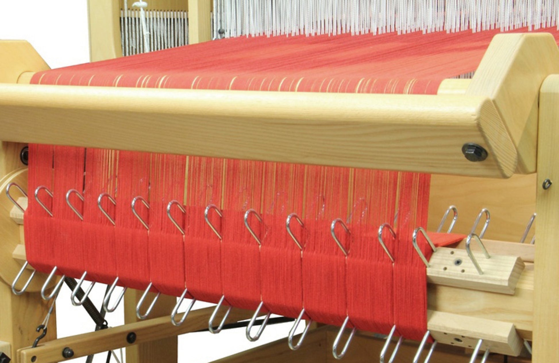 Close-up of a Louët Sectional Warp Kit for the Floor Looms with fine warps stretched across it. Metallic clips hold the bright red threads in place, and the intricate weaving apparatus from Louët Inc., including a Louët sectional warp beam, is visible in the background, showcasing the detailed machinery involved in the process.