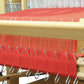 A close-up view of a Louët Inc. loom featuring rows of fine warps stretched tightly across the Louët Sectional Warp Kit for the Floor Looms, arranged in 1" or 2 cm sections. The threads are held securely by metal clips and are neatly organized on the sectional warp beam. The loom's wooden frame and heddles are visible, all set for the weaving process to begin.