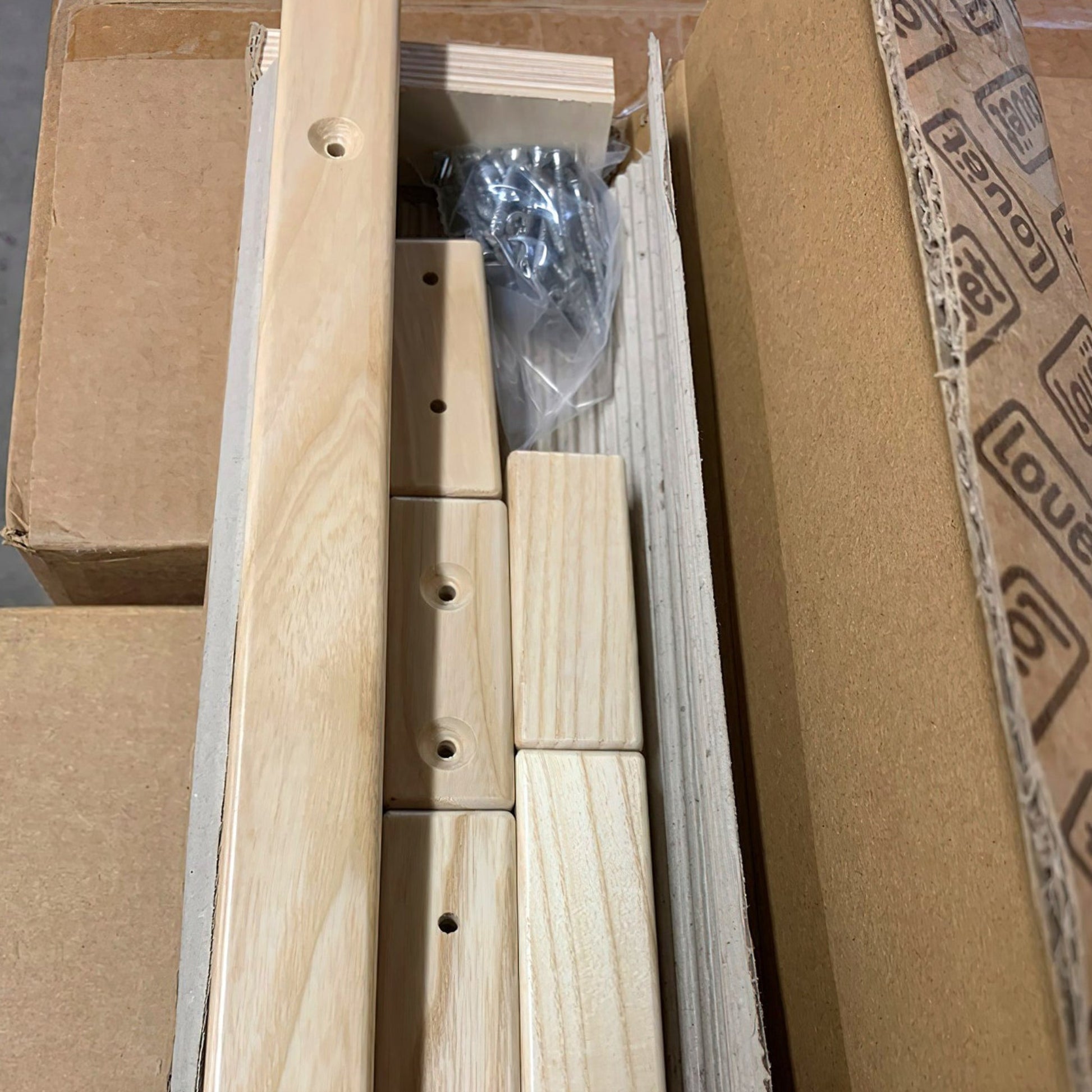 The Louët Delta Treadle Height Adjusting Kit by Louët Inc. arrives disassembled in a cardboard box, including rectangular wooden pieces with pre-drilled holes, screws neatly packed in a plastic bag, and other small components. All parts are meticulously arranged, ready for precise assembly.