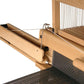 A close-up of a Louët Inc. floor loom with threads in place highlights the reed and heddles, essential parts of weaving, along with tensioned yarn. The natural wood finish contrasts beautifully with the white and black threads, and prominently features the Louët Fly Shuttle Device/Mechanism for efficient operation.