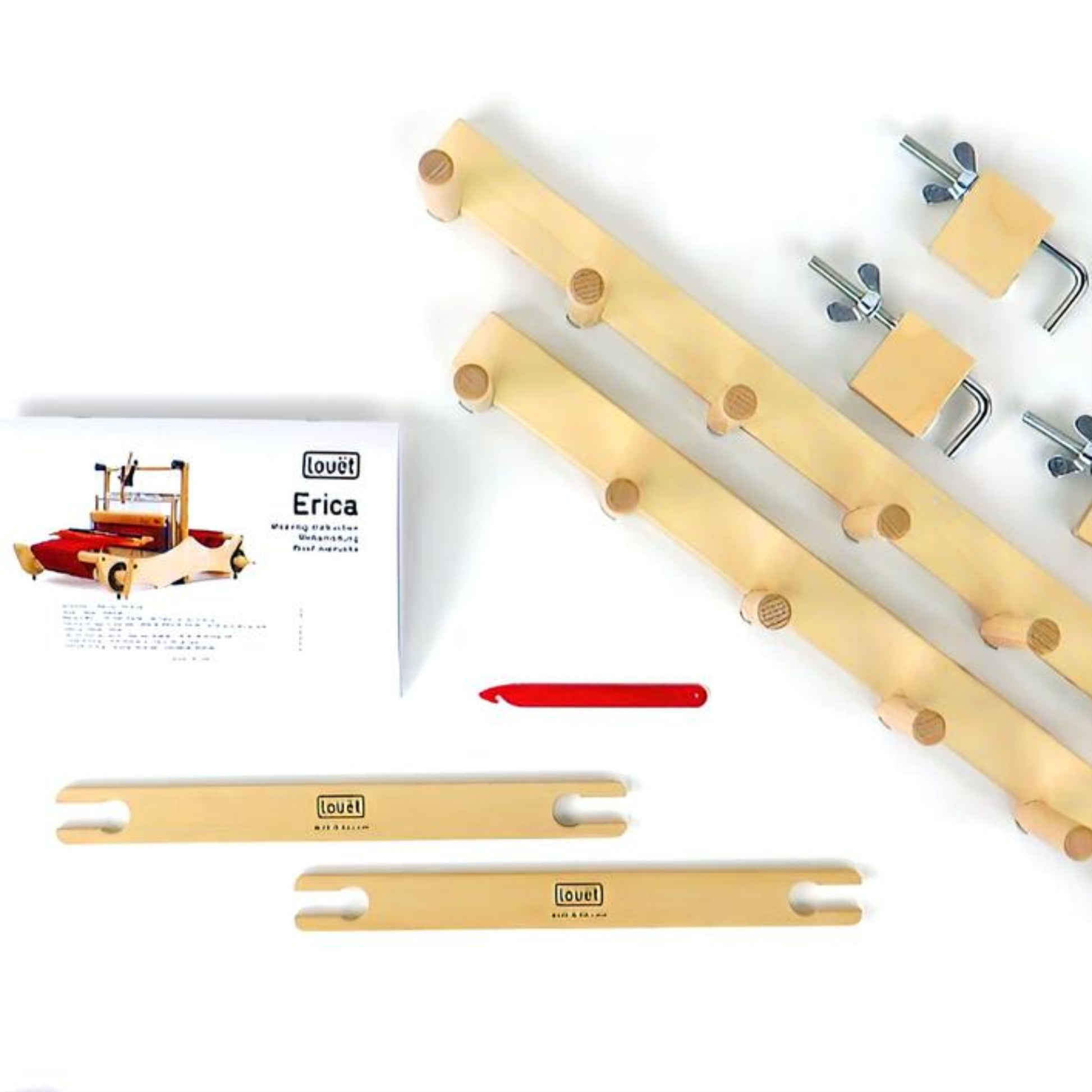 The image displays various wooden parts and clamps organized for assembling the Louët Erica Loom, part of the Louët Erica Accessory Package. Included in the package are a manual titled "Erica," a Texsolv reed, and a red tool. The light-finished wooden parts are labeled with "Louet," and warping posts ready for use are also visible.
