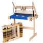 A wooden tabletop Jane Table Loom with a blue work surface is displayed. Next to it, a skein-winder holds black, yellow, and orange yarns wrapped around it. The equipment, including the Louët Loom Floor Stand by Louët Inc., is perfect for weaving textiles.