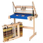 A Louët Loom Floor Stand from Louët Inc. stands proudly, showcasing a blue cloth partially woven on it. Beside the loom is a rectangular warping board with multicolored yarn wrapped around it, used for preparing the warp threads for weaving.