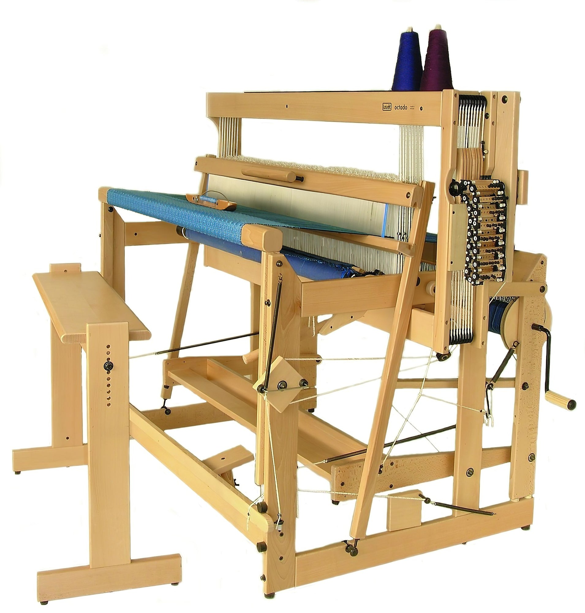 A Louët Octado 8-shaft Floor Loom without Dobby Control Head by Louët Inc. with blue fabric partially woven on it. The loom features various levers, pedals, and spools of thread, one purple and one blue, mounted on the right side. A small bench is positioned in front of the loom.