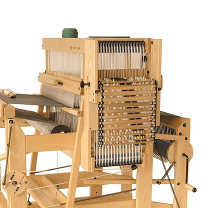 The Louët Megado Mechanical Dobby Head by Louët Inc. is a wooden weaving loom preloaded with threads and yarn, designed with multiple harnesses and heddles for creating intricate patterns. Its structure incorporates a beater bar and treadles, with a spool of green yarn placed on top, ready for use.