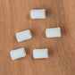 Five small, white plastic caps lay scattered on a wooden surface, resembling the intricate components of a Louët Inc. Louët Brake Tension Nut assembly.