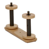 Introducing the Louët Lazy Kate - Rack with 2 Rods from Louët Inc., a wooden kinematic coupling featuring two vertical metal rods of different heights mounted on a rectangular wooden base. Reminiscent of Louët's Victoria spinning wheels, each rod features circular wooden disks on top and bottom, centered with a peg for rotating movement.