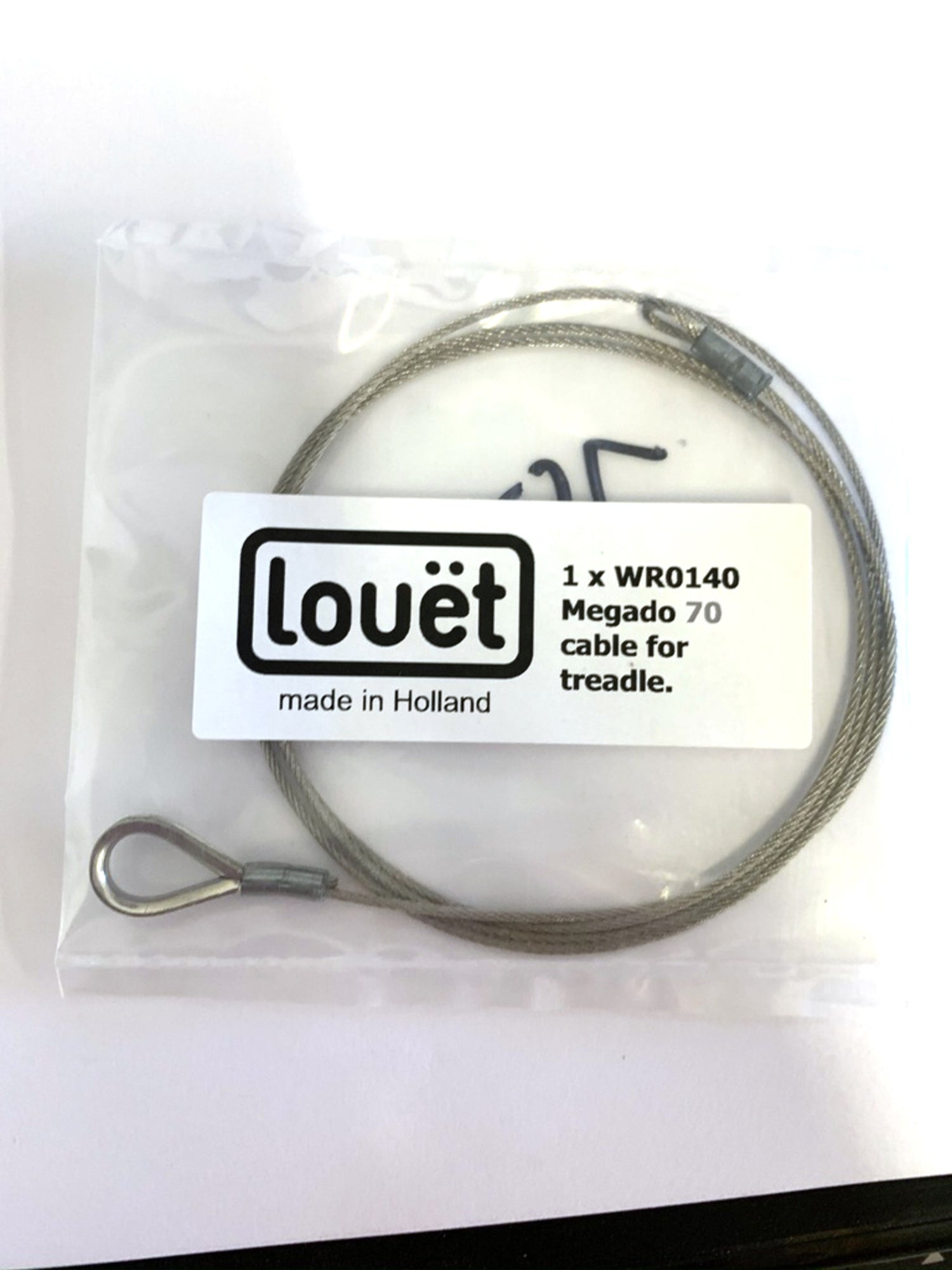 A coiled wire cable from Louët Inc. is inside a clear plastic bag. The label reads "Louët made in Holland" and "1 x WR0140 Megado 70 replacement treadle cable." Perfect for Louët Megado looms, the bag rests on a white surface.