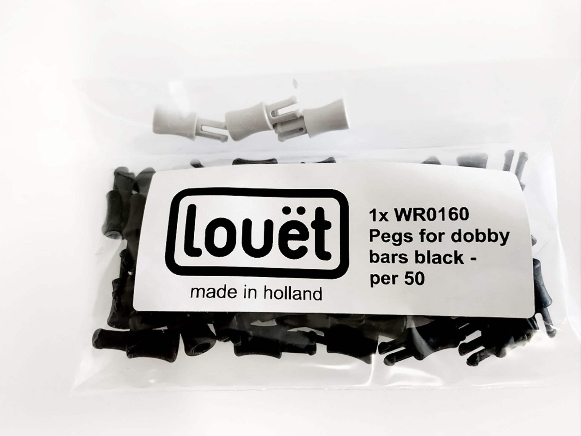 A clear plastic bag containing black pegs for a dobby loom is labeled "Louët Inc., made in Holland." The label also reads "1x Louët Pegs for Dobby Bars (set of 50)." Several pegs and two rod-shaped items are visible inside the bag.