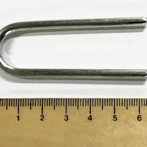 A Louët metallic U-bolt lies on a white surface next to a wooden ruler. The ruler's measurements indicate the U-bolt's length is approximately 6 centimeters, while Louët Metal Clips for Sectional Warping, packed fifteen to a pack, are scattered nearby, hinting at some ongoing project by Louët Inc.