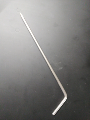 A Louët Weaving Loom Blocking Pin, a silver L-shaped metal rod by Louët Inc., with one end slightly pointed, laying on a dark surface.