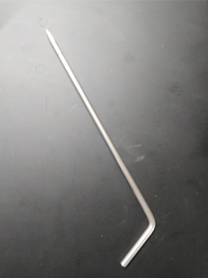 A Louët Weaving Loom Blocking Pin, a silver L-shaped metal rod by Louët Inc., with one end slightly pointed, laying on a dark surface.