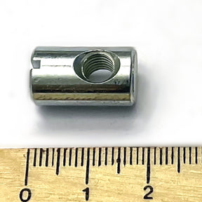 A small, cylindrical metal Louët M6 barrel nut with a threaded hole in the center, from Louët Inc., is placed beside a wooden ruler. The ruler's markings indicate that the 6 mm size nut is approximately 1 centimeter in length. The background is white.