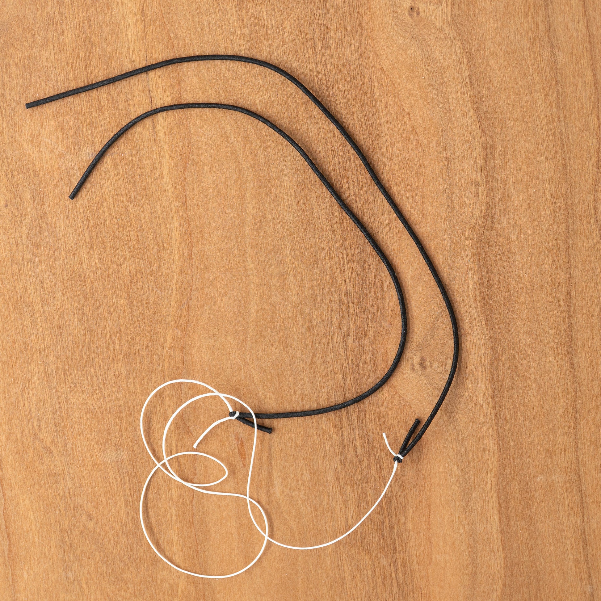 A black shoelace tied in a double knot with another black and white shoelace, resembling the Louët S10C Scotch Tension Brake Cord by Louët Inc., placed on a wooden surface.