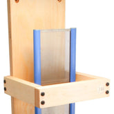 A close-up of the Harrisville Designs Reed Stand/Rack for hair-building fibers shows a tall base made of Baltic birch plywood and a rectangular wooden frame with a blue metal comb in the center. The structure, resembling a reed rack, is secured with screws at the corners.