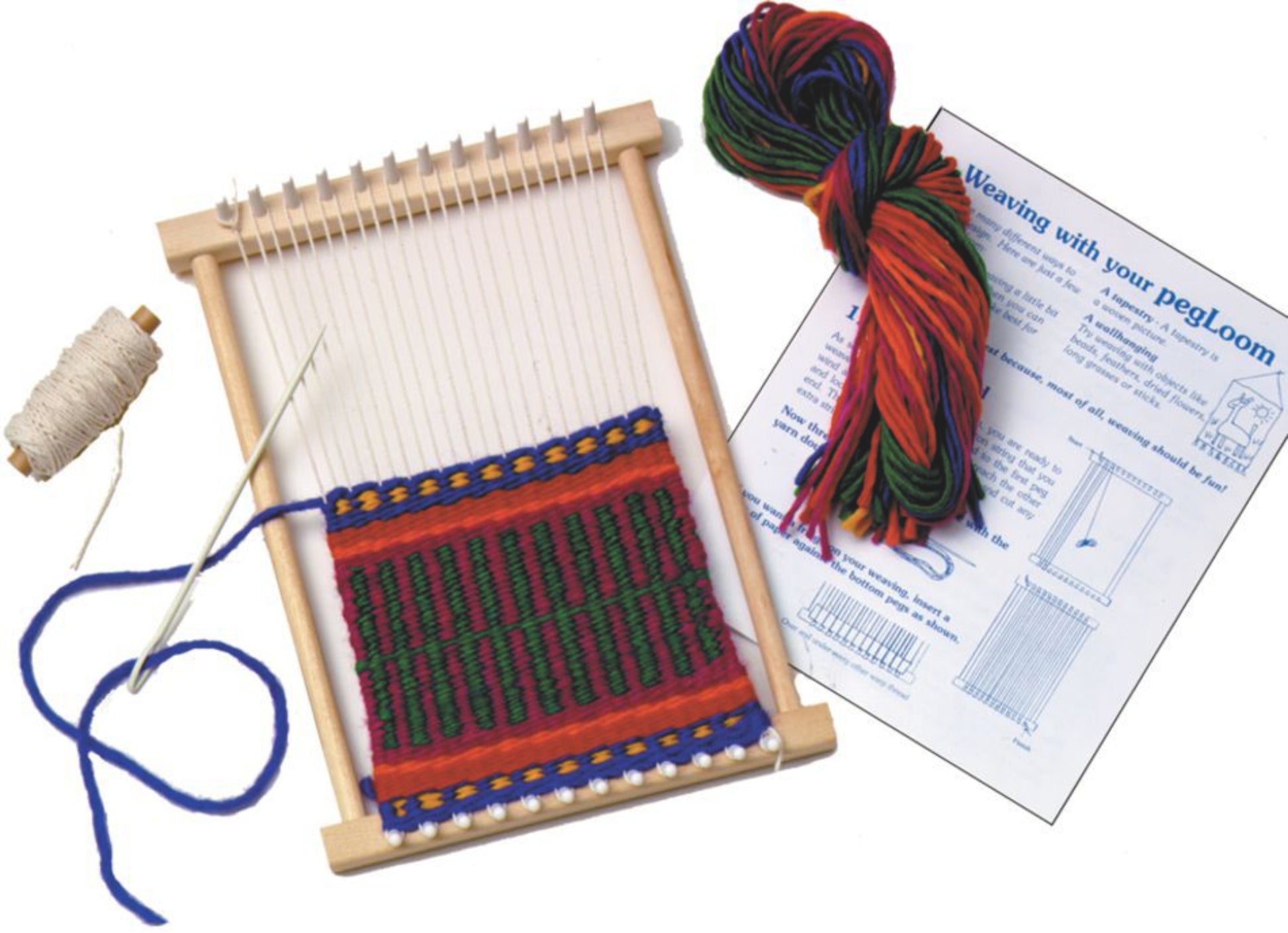 A small Harrisville Designs Peg Loom with a partially completed design in red, green, and yellow yarn. Nearby are a skein of multicolored yarn, a needle with blue thread, a spool of white string, and an instructional booklet titled "Weaving with Your PegLoom." Perfect for kids weaving projects.