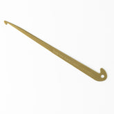 The Halcyon's Engraved Brass Hook for Threading and Sleying by Harrisville Designs is a long, slender, L-shaped tool made of brass with a hooked end and a small hole near the opposite end. The brass hook is laying on a white surface and features engraved text.