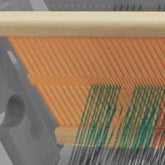 Close-up image of a section of a Glimakra Emilia Rigid Heddle Reed with orange and green threads running through the wooden frame. The loom parts, including heddles, are partially visible, showcasing the threads being woven together.