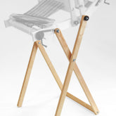 A pair of wooden folding legs from the Glimakra Emilia Rigid Heddle Loom - Floor Stand stand against a plain white background. Specifically designed to support the Emilia rigid heddle loom for weaving, the supported object is faded out and unclear. The legs feature metal hinges for convenient folding.