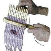 Hands weaving lilac-colored yarn on a Lacis 12 Stick Walking Stick-Loom. The walking stick-loom from Lacis is held in one hand while the other guides the yarn through the threads, effortlessly creating a patterned tapestry weave.