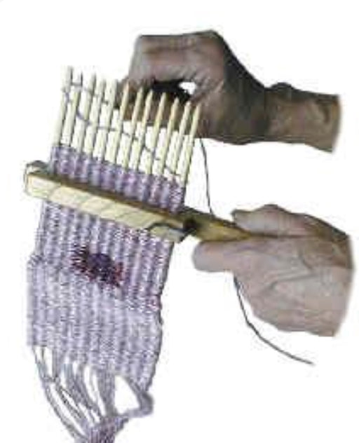 Hands weaving lilac-colored yarn on a Lacis 12 Stick Walking Stick-Loom. The walking stick-loom from Lacis is held in one hand while the other guides the yarn through the threads, effortlessly creating a patterned tapestry weave.