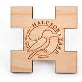 The Weaving Sett Tool by Halcyon Yarn, crafted from wood in the shape of a plus sign, features a bird design with "Halcyon Yarn" engraved at the center. It also includes engravings of "Yarn Fiber Tools" and "Since 1971" around the bird design—making it an ideal tool for weaving samples and testing for shrinkage.