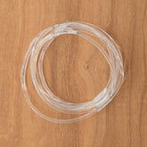 A coiled transparent tube, similar to the Ashford Country Spinner - Poly Drive Band by Ashford Handicrafts Limited, is neatly arranged on a wooden surface, ready for use.