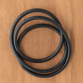 A black Ashford Drum Carder Drive Band, resembling a rubber O-ring, coiled on a wooden surface.