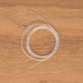 A coil of clear fishing line is neatly wound on a wooden surface, showcasing the precision of an Ashford Scotch Tension Brake Band by Ashford Handicrafts Limited.