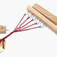 The Leonardo Rope Maker & Yarn Twister by Lacis is displayed. It features a handmade wooden loom with a rectangular base equipped with nails, several red threads that extend from it and are hooked to a circular wooden disk. A small rectangular wooden piece is attached to the disk, functioning as a rope maker.