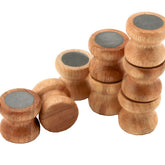 A group of small, wooden, cylindrical objects are arranged in a line. Several Lacis Kumihimo Tamas (Bobbins) made from hardwood are stacked on top of each other at varying heights. The tops of these bobbins are flat and feature circular, gray, metallic centers.