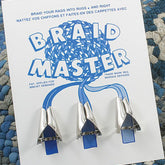 An instructional sheet titled "Braid Master" from the BraidAid collection by Halcyon Yarn features a set of three metal braid-making tools and comes with a reversible rug for added style. The instructions, provided in both English and French, will guide you in mastering this versatile braiding device.