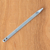 A tent stake from Halcyon Yarn's Braidkin Lacer line, featuring a pointed end and two holes at the other end, rests on a wooden surface.