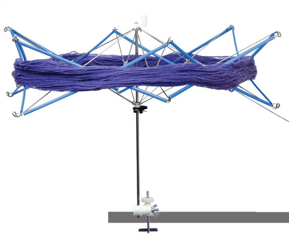 A Lacis Plastic and Metal Swift/Skein Winder with a skein of purple yarn wrapped around it. The device, featuring blue arms and a central pole for winding skeins, is mounted on an adjustable clamp that attaches to the edge of a table or surface.