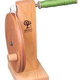 An Ashford Boat Shuttle Bobbin Winder Wooden with a natural wooden finish from Ashford Handicrafts Limited. The device features a large wooden wheel on one side and a stainless steel shaft with nylon bearings supporting the spool of green yarn on the other. Its sturdy base provides stability during use, and the logo reads "Ashford New Zealand.