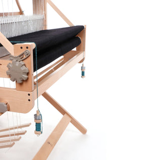 A close-up image of a wooden weaving loom with black fabric in progress. The loom features various wooden components, including gears and spindles with blue and white thread. Ashford Warp Thread Weights by Ashford Handicrafts Limited are neatly arranged among the warp threads, showcasing the intricate structure against a clean white background.