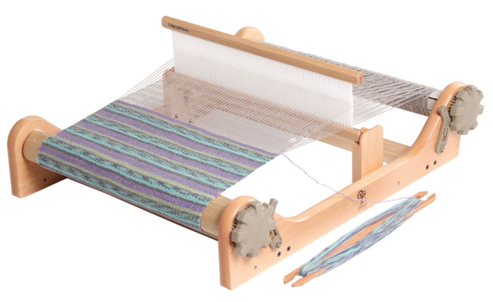 An Ashford Rigid Heddle Loom by Ashford Handicrafts Limited with partially woven fabric in shades of blue, green, and purple. The portable wooden loom is equipped with horizontal bars and side gears, with threads stretched across it. A shuttle carrying thread is placed near the loom, making it perfect for hand weaving enthusiasts.