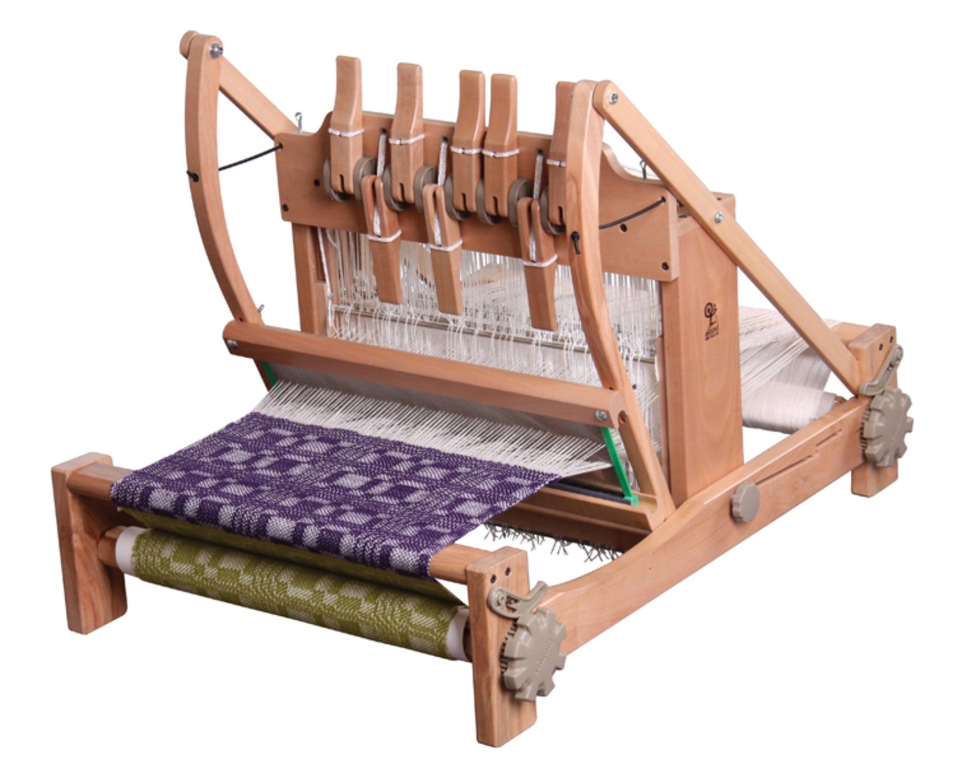 An Ashford Handicrafts Limited Table Loom, featuring an overhead/swinging beater and Texsolv heddles. It is set up with white warp threads and showcases multiple levers for easy operation. The loom has a partially completed purple and white woven fabric on the upper section and a green and white woven fabric rolled up on the lower section.