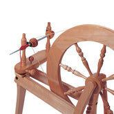 Presenting the Ashford Quill Spindle by Ashford Handicrafts Limited: a wooden spinning wheel featuring a large circular wheel with multiple spokes and a spindle actively spinning wool roving into yarn, all mounted on a sturdy wooden frame.