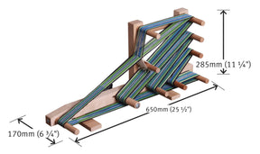 An Ashford Inkle Loom by Ashford Handicrafts Limited, crafted from wood and featuring multiple pegs that hold tightly woven green and blue threads in place. Ideal for creating warp-faced straps, its dimensions are 285mm in height, 650mm in length, and 170mm in width.